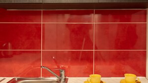 A kitchen with dark wooden cabinets, a stainless steel sink, and red-tiled backsplash. - Comfort Apartments 2 (Heraklion)