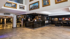 A spacious lobby with a high ceiling, a reception desk, and multiple framed artworks on the walls. - Hotel Bariloche Suites (San Carlos de Bariloche)