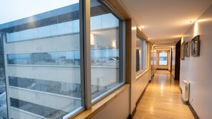 A modern hotel corridor with large windows, wooden flooring, and framed pictures on the walls. - Hotel Bariloche Suites (San Carlos de Bariloche)