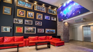 A lobby with a red sectional sofa, a flat-screen TV on the wall, and framed pictures. - Hotel Bariloche Suites (San Carlos de Bariloche)