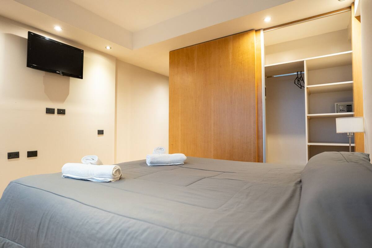 Una habitación de hotel moderna con una cama grande, un televisor de pantalla plana montado en la pared y un vestidor con estantes.
