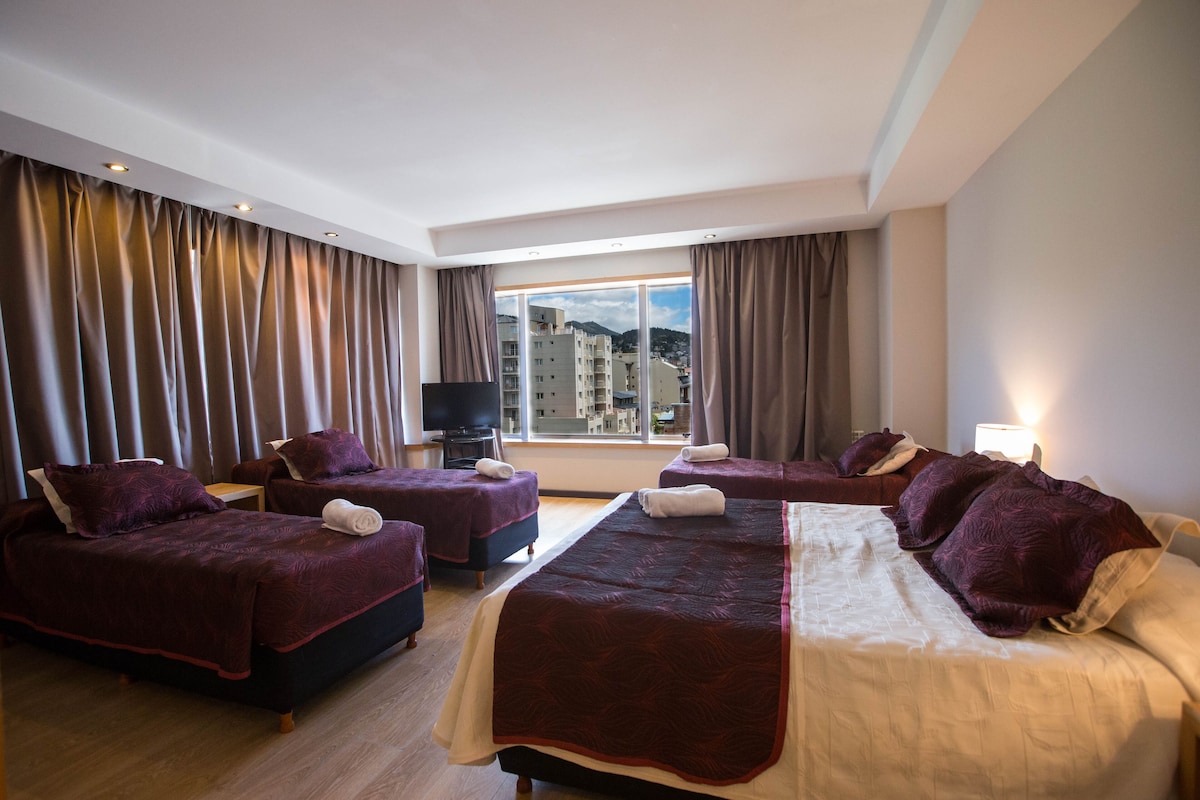 Habitación de hotel con dos camas, un televisor y un ventanal con cortinas.