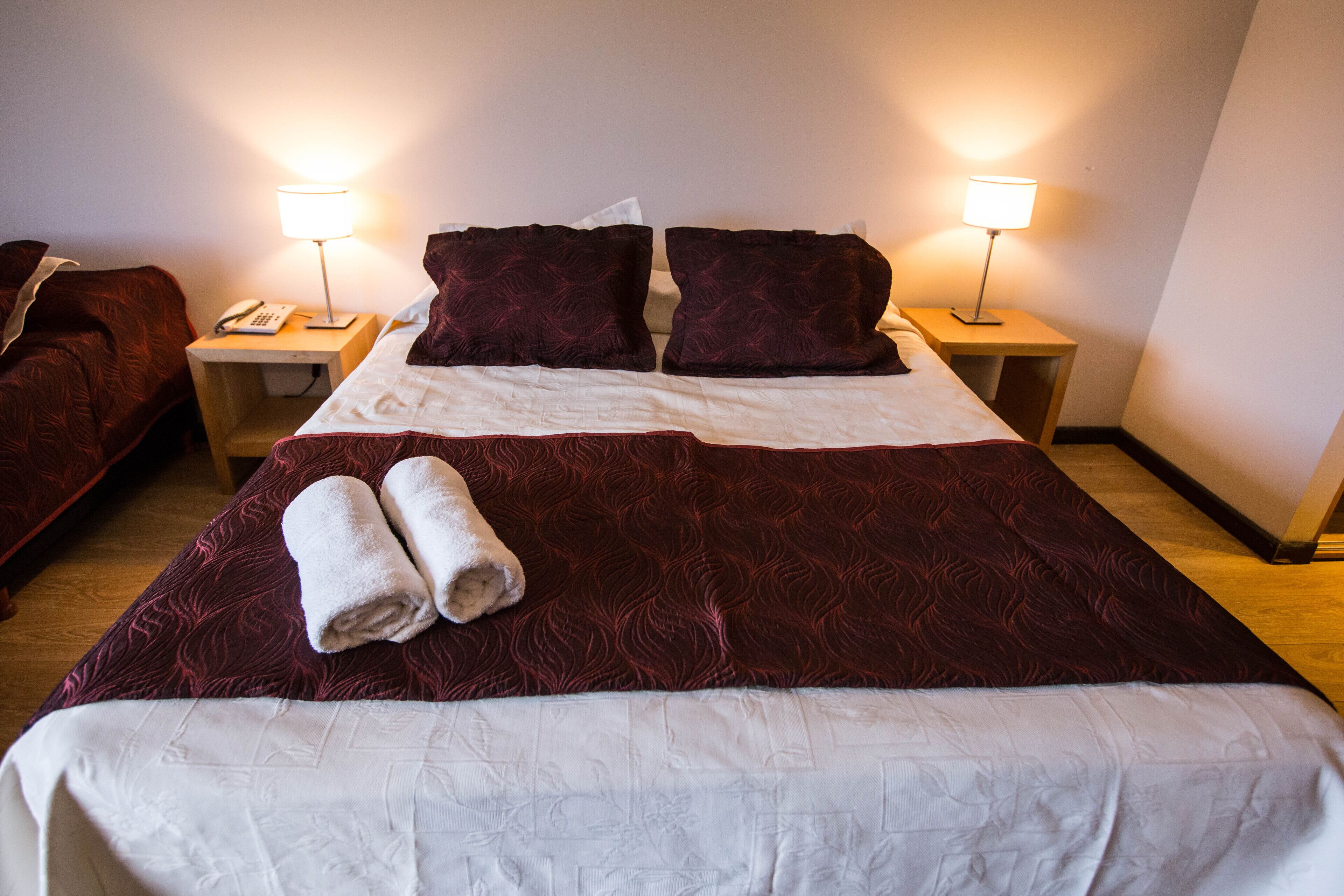 A hotel room with a large bed, two bedside lamps, a telephone, and neatly folded towels.