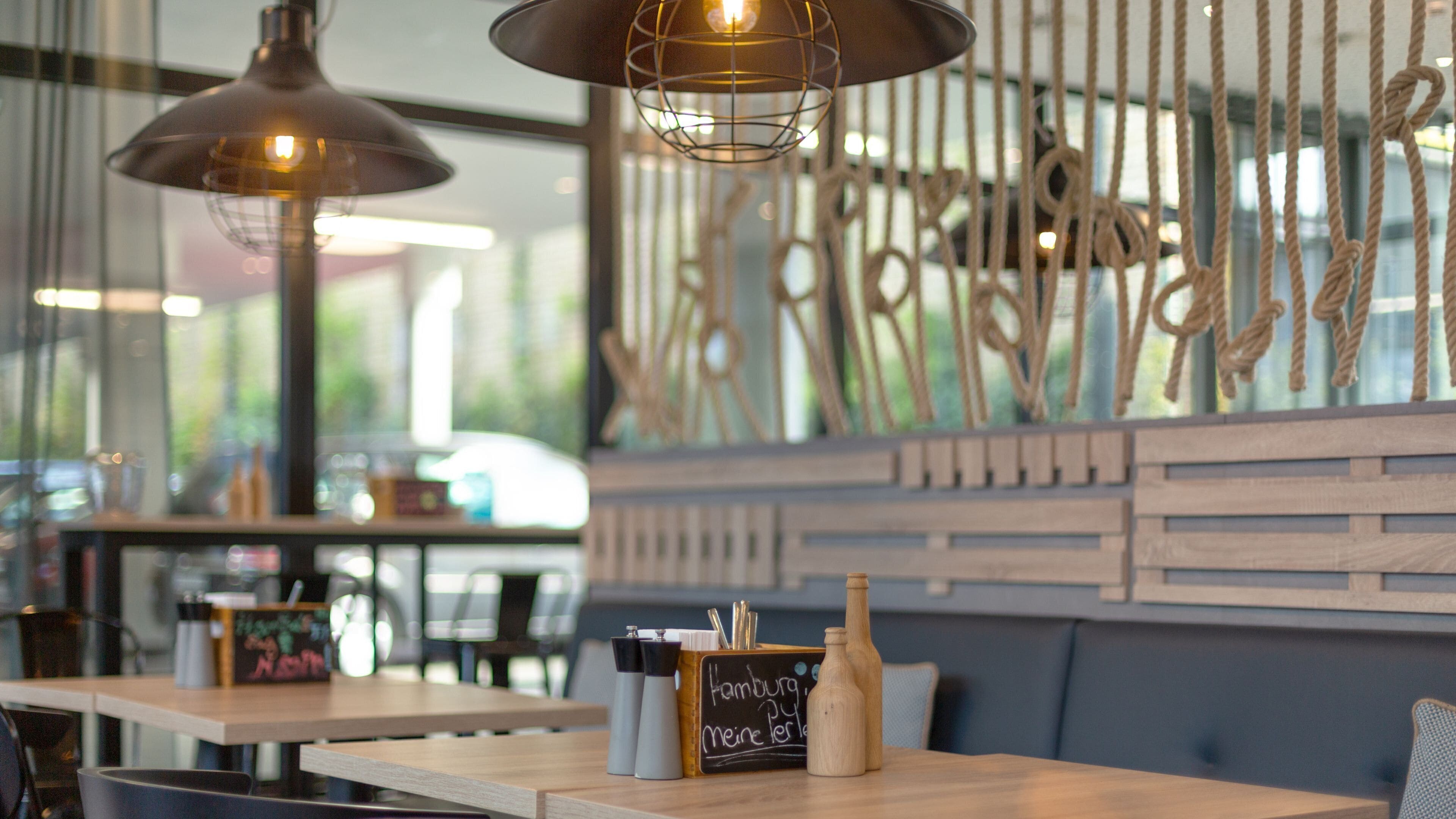 A restaurant interior with wooden tables, hanging pendant lights, and a decorative wall with vertical elements.