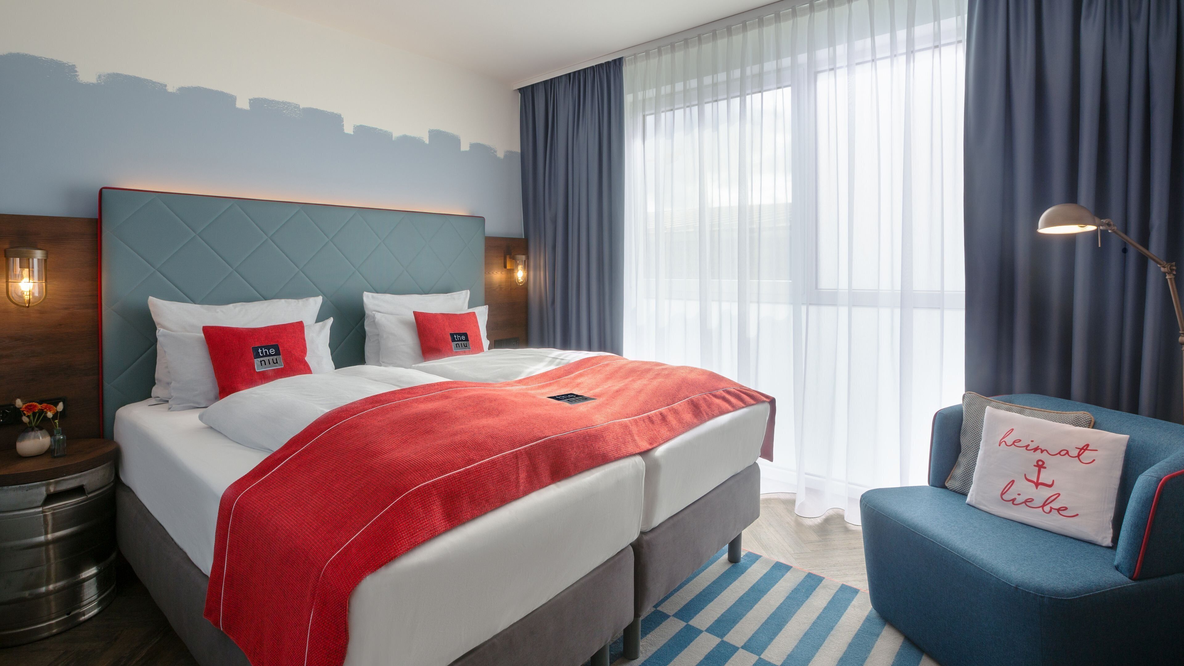 A hotel room with a bed, a nightstand, a lamp, a chair, and a window with curtains.