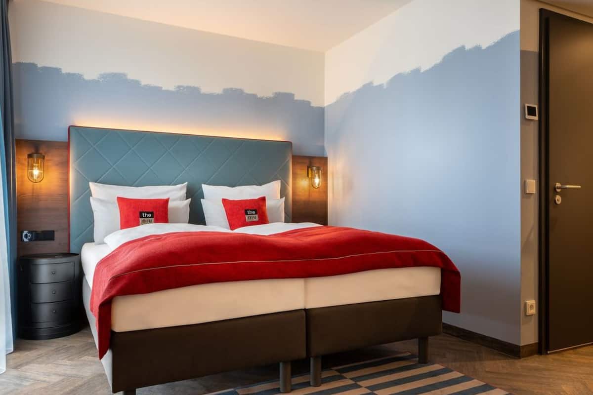 A modern hotel room with a bed, a nightstand, a dresser, and a door.