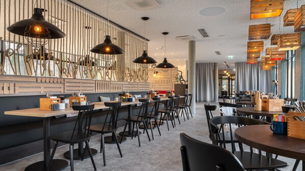 A modern restaurant interior with high ceilings, exposed ductwork, and a mix of wooden and metal furniture.