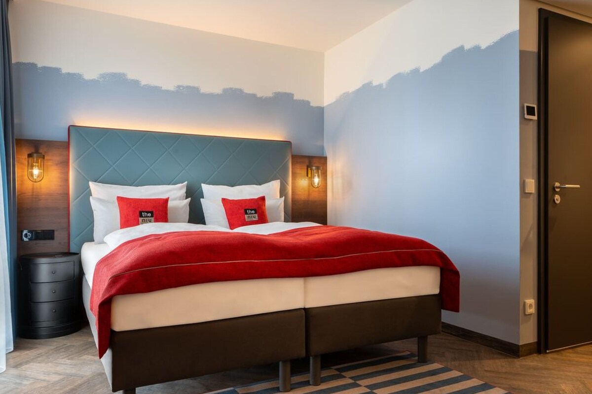 Una habitación de hotel moderna con una cama, una mesita de noche, un aparador y una puerta.