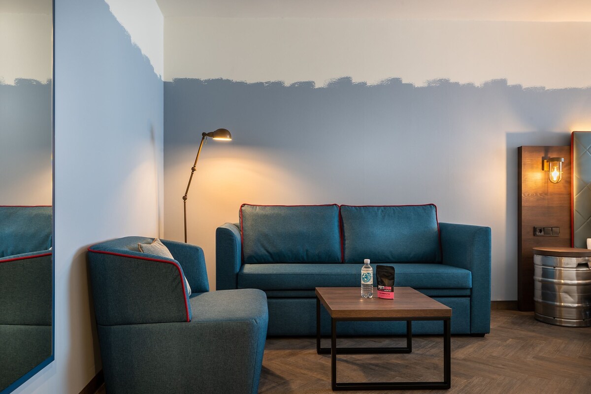 Una sala de estar moderna con un sofá azul, un sillón a juego, una mesa de centro de madera y una lámpara de pie.