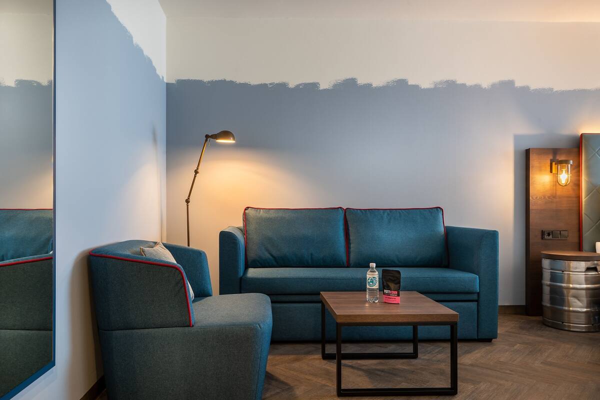 A modern living room with a blue sofa, a matching armchair, a wooden coffee table, and a floor lamp.
