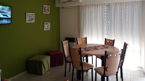 Een eetruimte met een ronde tafel, stoelen, een televisie en een raam met gordijnen.