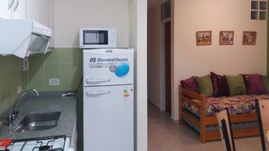 Een kleine keuken met een magnetron en een koelkast, een eethoek met een tafel en stoelen, en een bank met kussens.