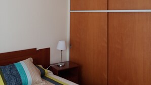 Hotelkamer met een bed, een houten garderobe, een nachtkastje met een lamp en een plafondlamp.