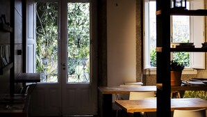 A dining area with a wooden table and chairs, a potted plant, and a view of greenery through a door with decorative metalwork. - Pensión O Xardin de Julia (Santiago de Compostela)