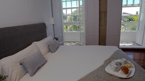 A bedroom with a large bed, a breakfast tray, and a view of greenery through open windows. - Pensión O Xardin de Julia (Santiago de Compostela)