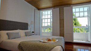 A bedroom with a large bed, a breakfast tray, and a view of greenery through the windows. - Pensión O Xardin de Julia (Santiago de Compostela)
