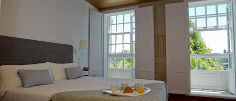 A bedroom with a large bed, a breakfast tray, and a view of greenery through the windows.