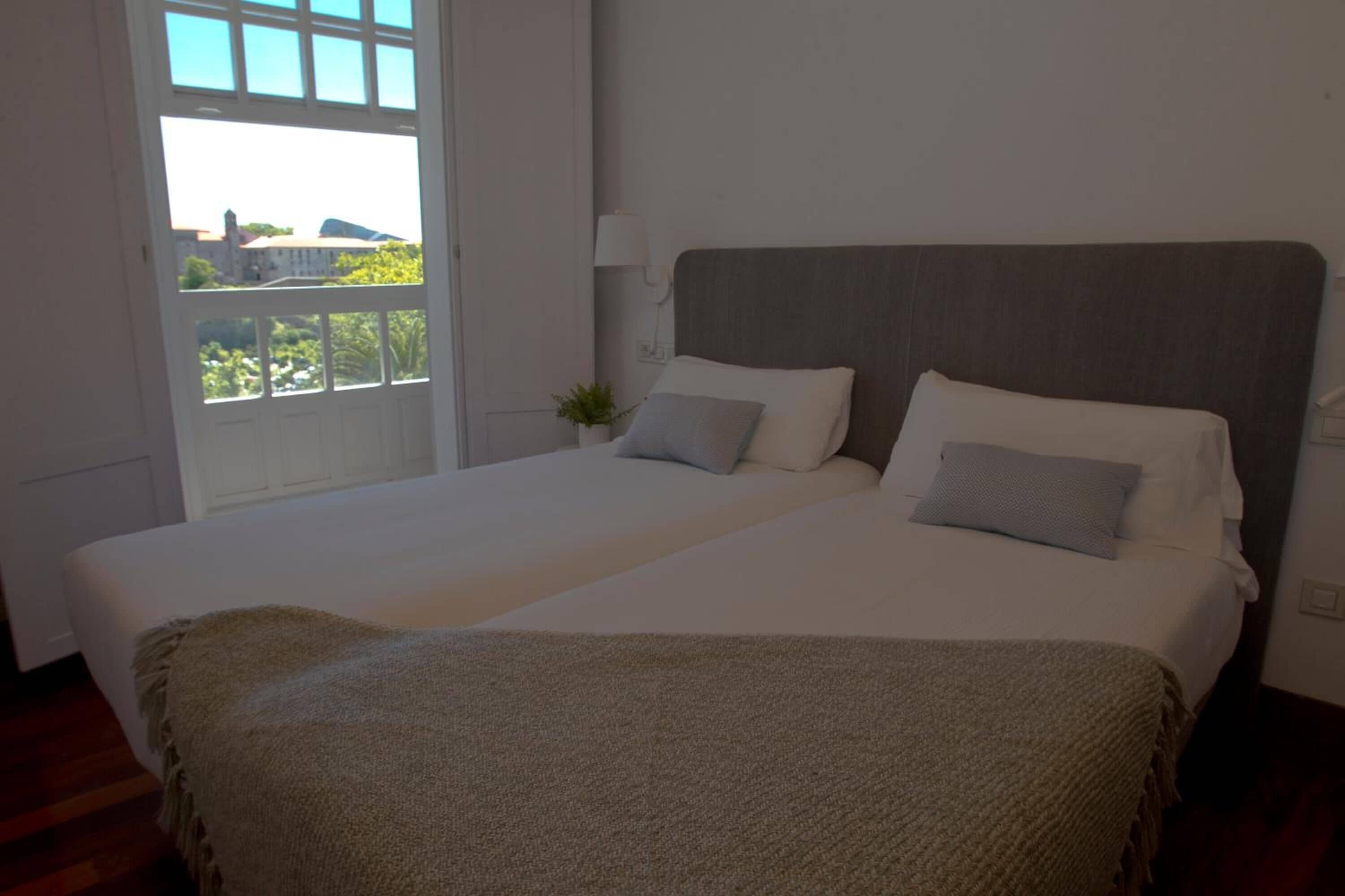 A bedroom with a large bed, a window with a view, and a bedside table with a lamp.