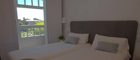 A bedroom with a large bed, a window with a view, and a bedside table with a lamp.