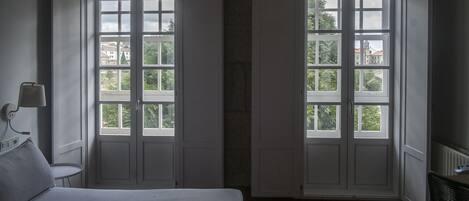 Una habitación con una cama, dos ventanas, un radiador y una silla.