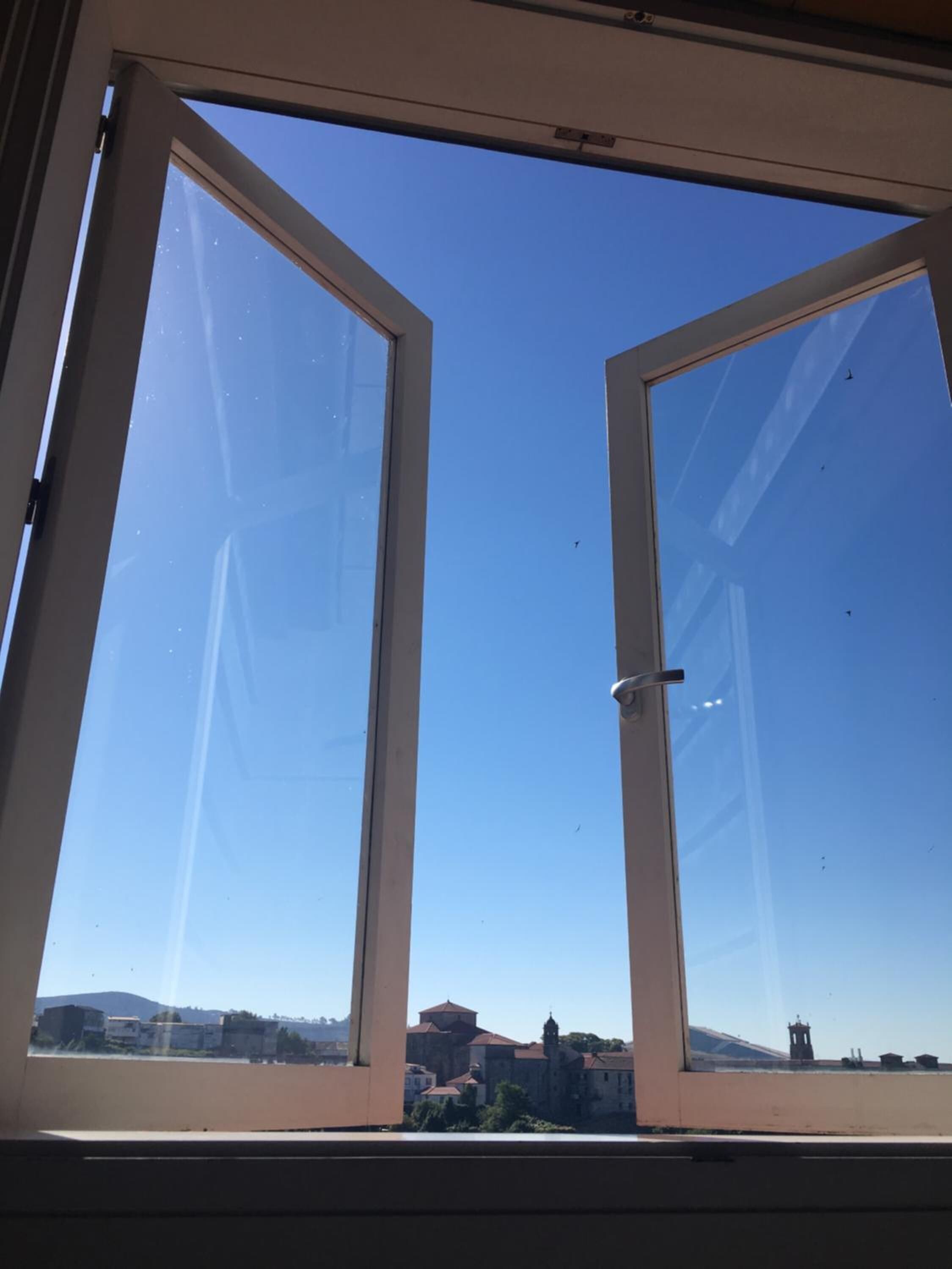 Un ciel dégagé vu à travers une fenêtre, avec des bâtiments et une tour qui se dessinent au loin.