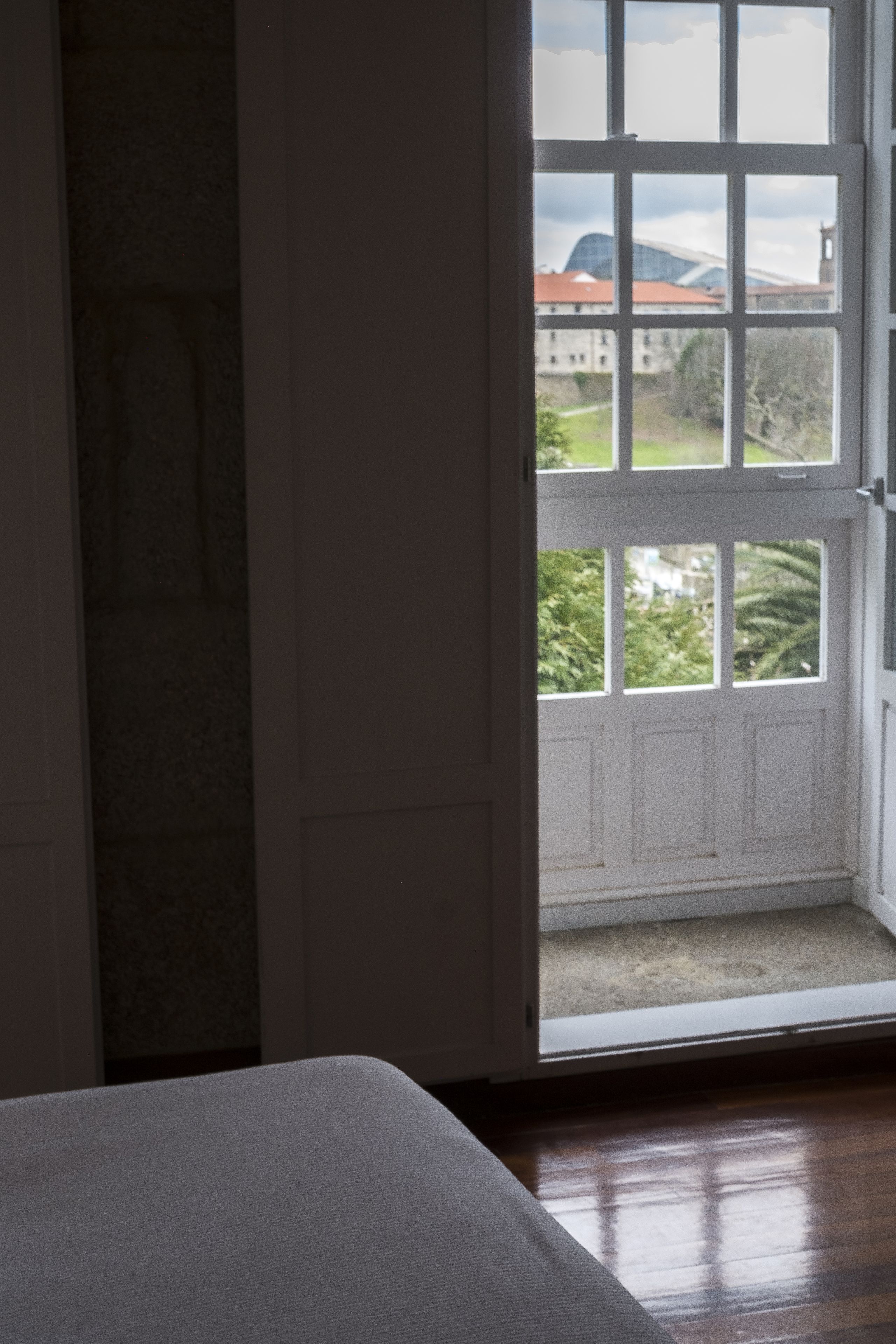 Una habitación con piso de madera, una puerta blanca que da a un espacio exterior con vistas a edificios y árboles.