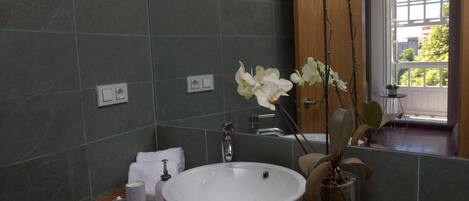 Un baño con un lavabo grande blanco, un espejo y un jarrón con orquídeas blancas.