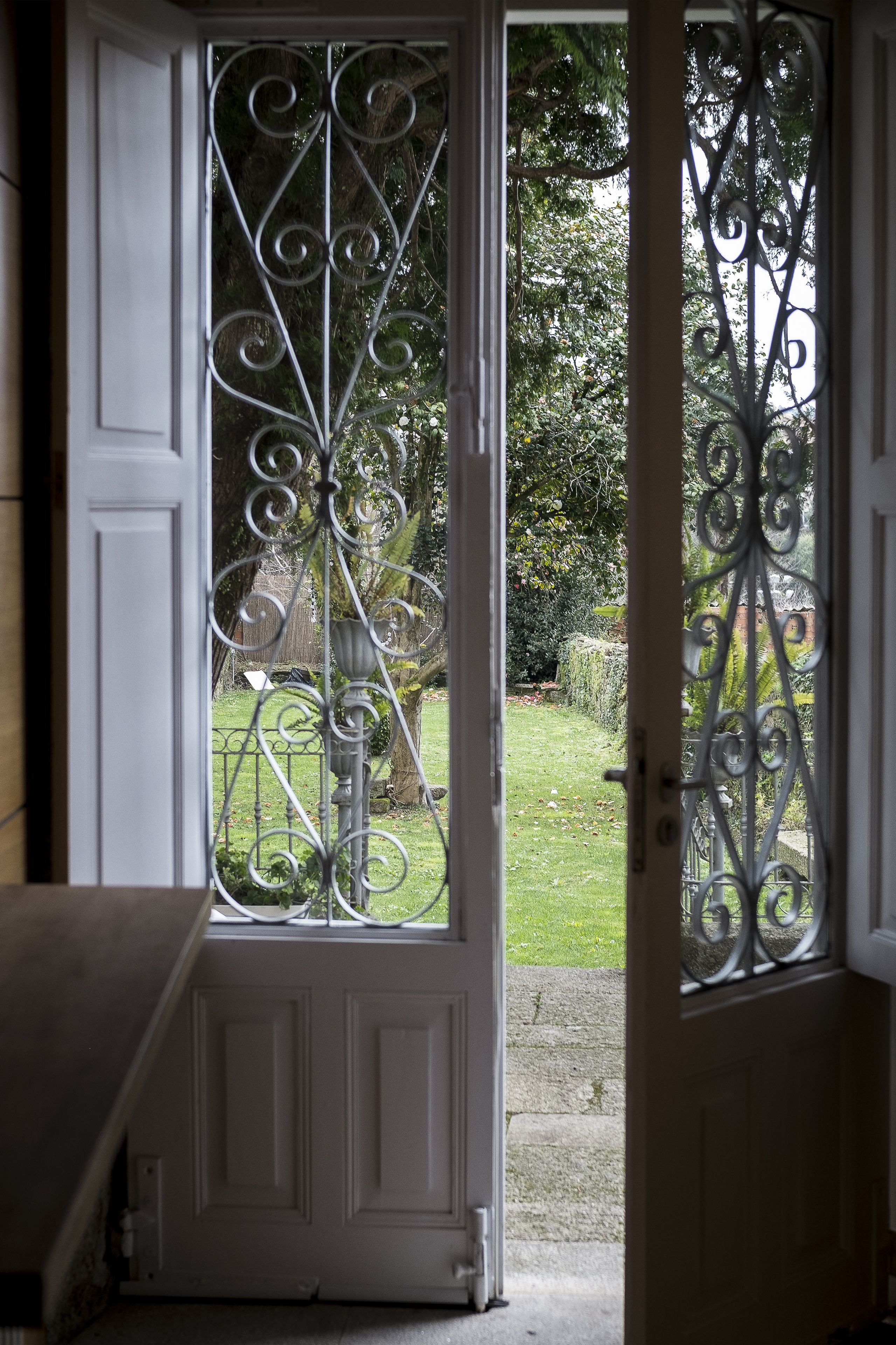 A white door with ornate metalwork and a view of a well-maintained garden.