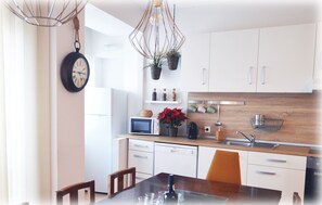 A modern kitchen with white cabinets, a microwave, a sink, and a dining area with a table and chairs. - Country Apartment by JC (Porto)