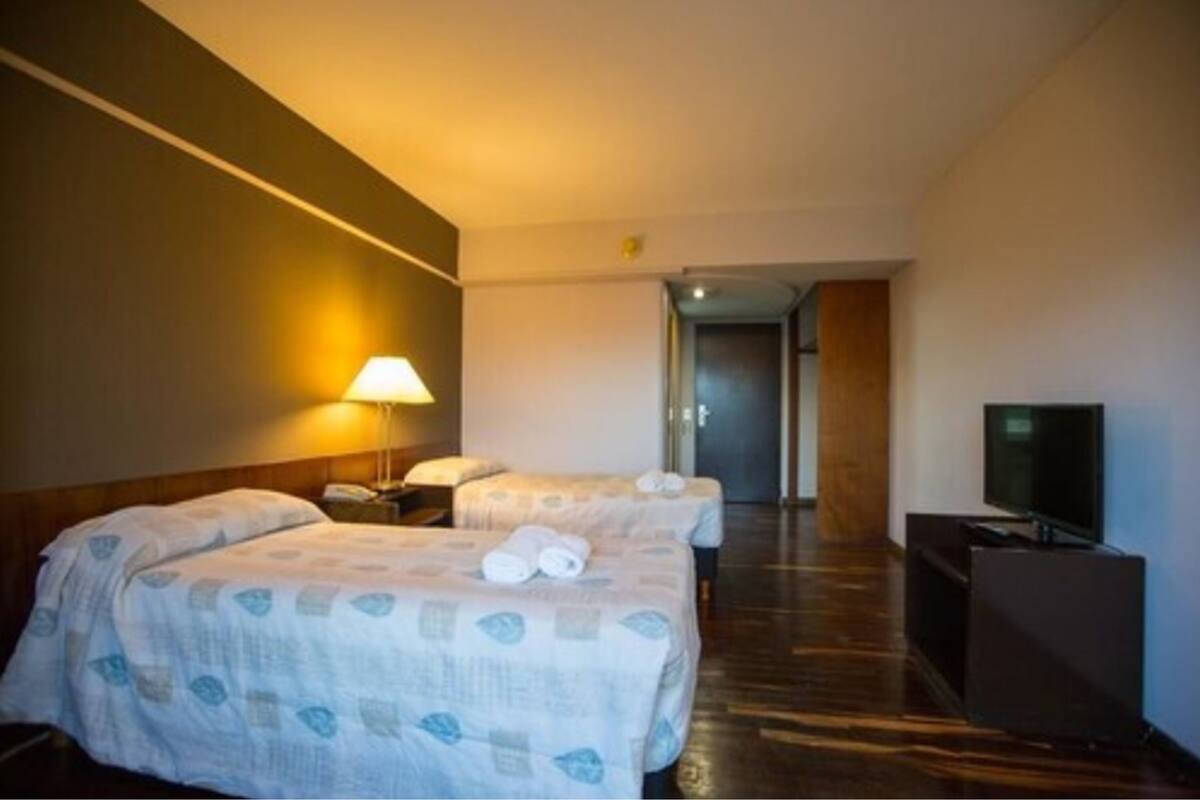 Une chambre d’hôtel avec deux lits, une télévision, une lampe et un plancher en bois.