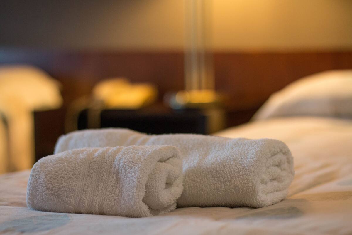 Un lit bien fait, avec deux serviettes blanches roulées et une lampe en arrière-plan.