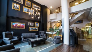 En rymlig entréhall med en svart vägg dekorerad med inramade fotografier, en kristallkrona och ett stort soffbord. En trappa med glasräcken leder upp till en övre våning.