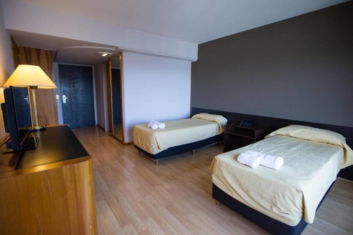 Une chambre d’hôtel avec deux lits, un bureau, une lampe et une porte donnant sur une autre pièce.