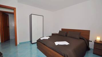 Un dormitorio con cama de madera, mesita de noche, lámpara de noche, armario y suelo de baldosas.