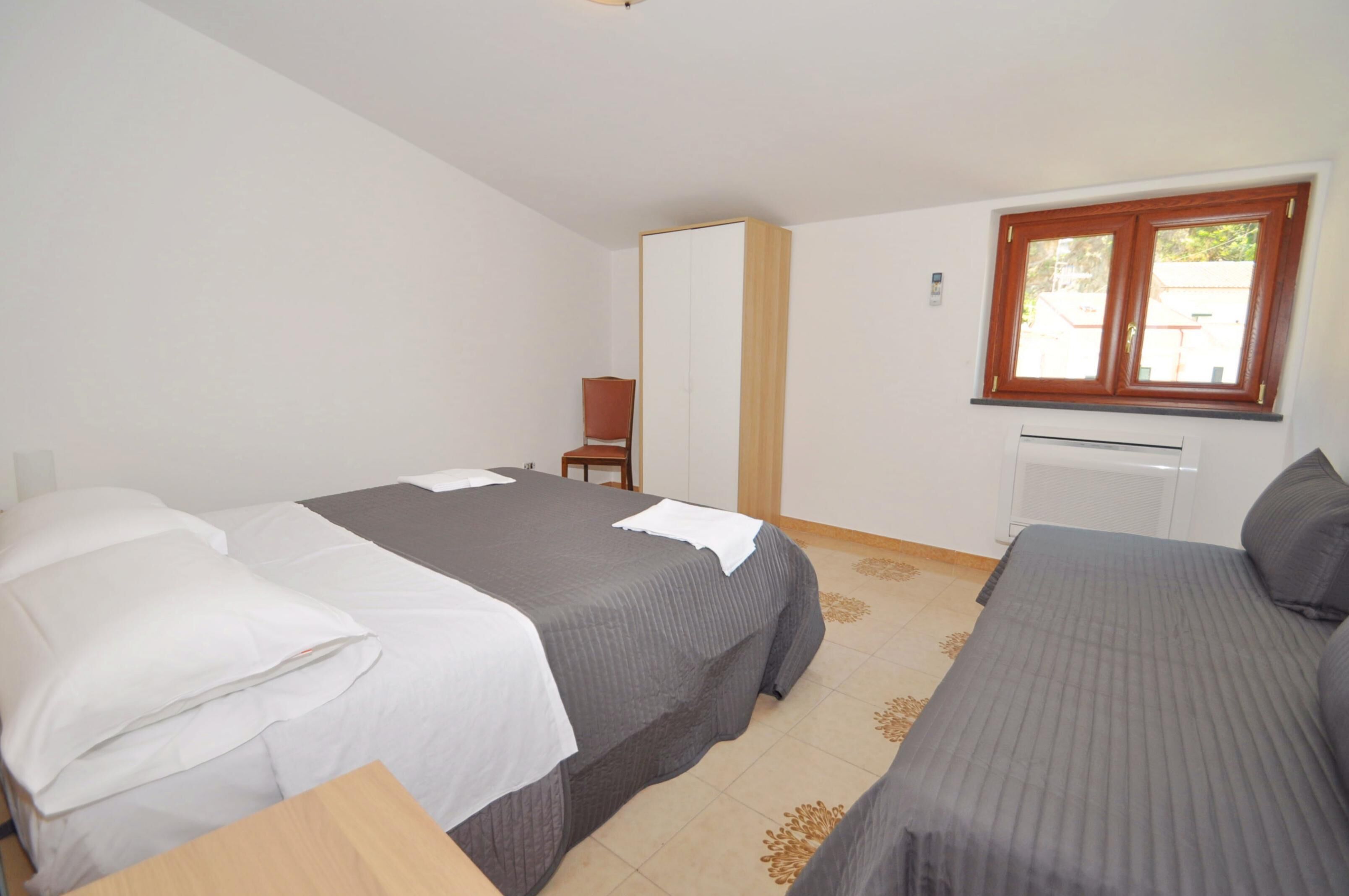 A room with two beds, a wardrobe, a chair, and a window.