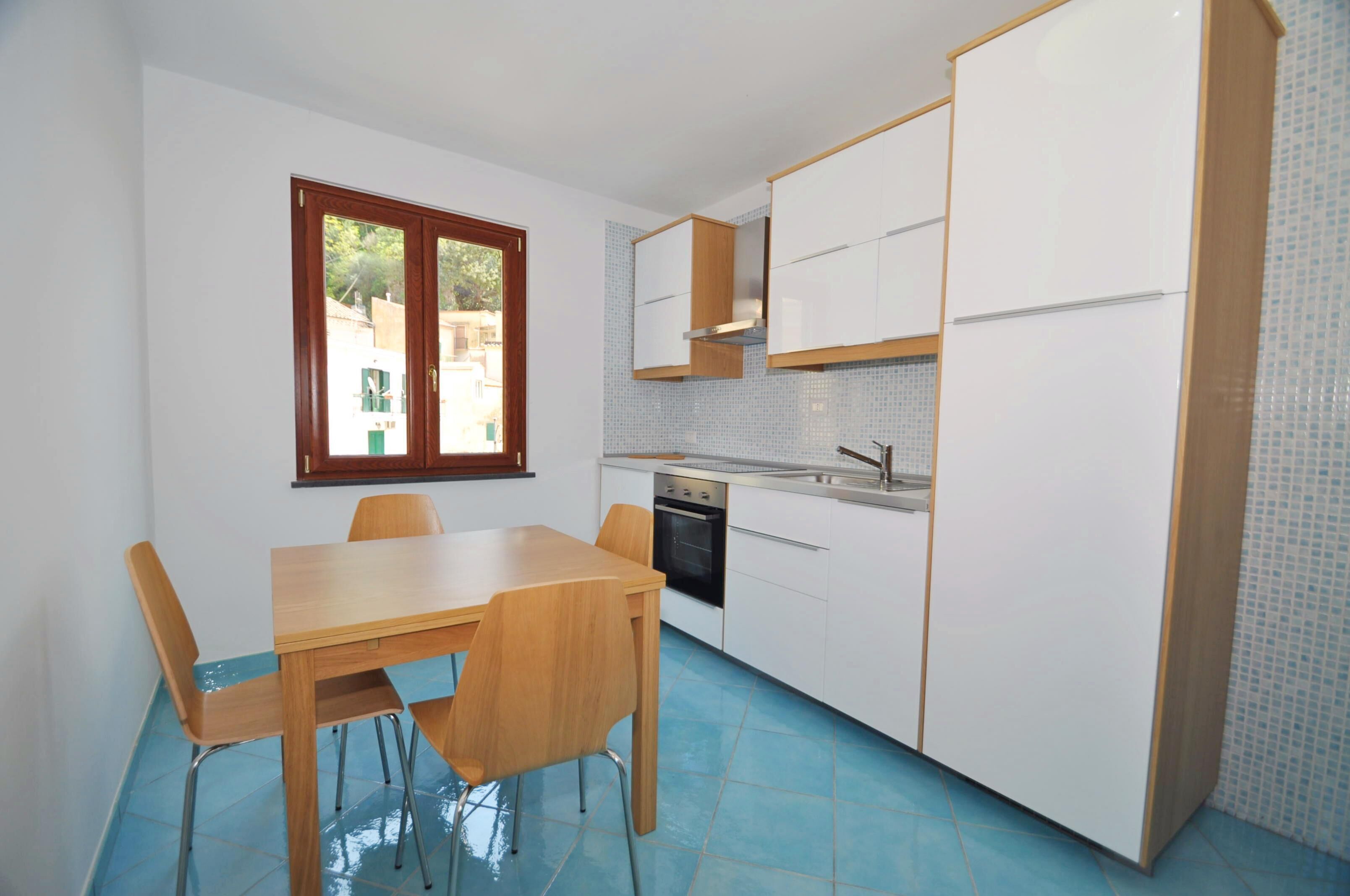 Een kleine keuken met een eettafel en stoelen, een raam en een betegelde spatwand.