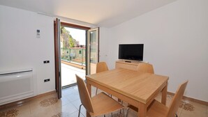 A dining area with a wooden table and chairs, a television on a stand, and a sliding glass door leading to an outdoor balcony. - Apartments Cetara (Cetara)