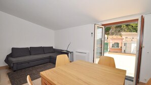 A modern living room with a grey sofa, a wooden dining table, and a view through a glass door to the outside. - Apartments Cetara (Cetara)