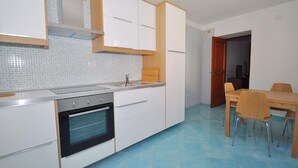 A kitchen with white cabinets, a built-in oven, and a dining area with a wooden table and chairs. - Apartments Cetara (Cetara)
