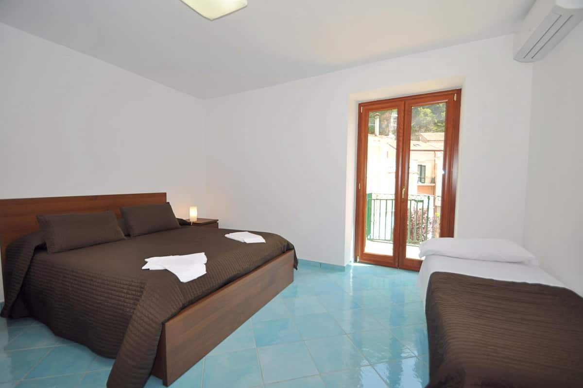 A bedroom with a large bed, a smaller bed, and a balcony with a view.
