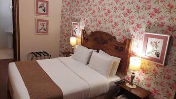 A neatly made bed with white linens and a brown striped blanket, a wooden headboard, two bedside lamps, a nightstand with a telephone, and floral wallpaper.