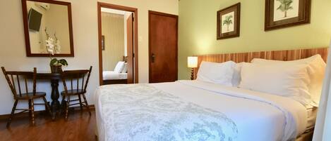 Una habitación de hotel con una cama grande, una silla de madera, una mesita pequeña y un espejo.