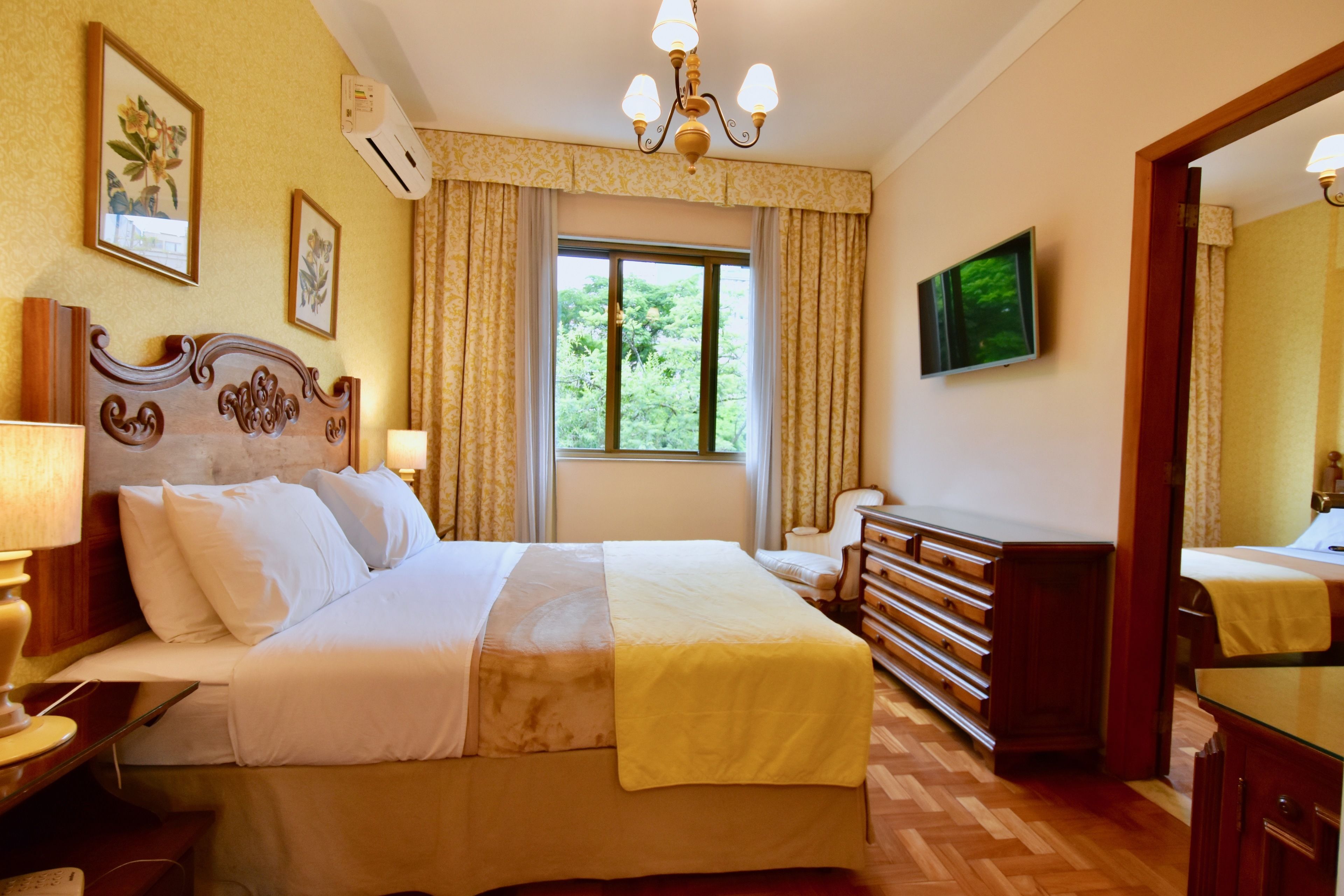 Une chambre d’hôtel avec un grand lit, une commode en bois, une télévision et une fenêtre avec des rideaux.