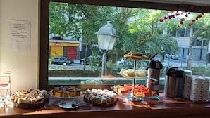 Un buffet de petit-déjeuner proposant diverses pâtisseries et desserts, une machine à café et une vue sur la rue.