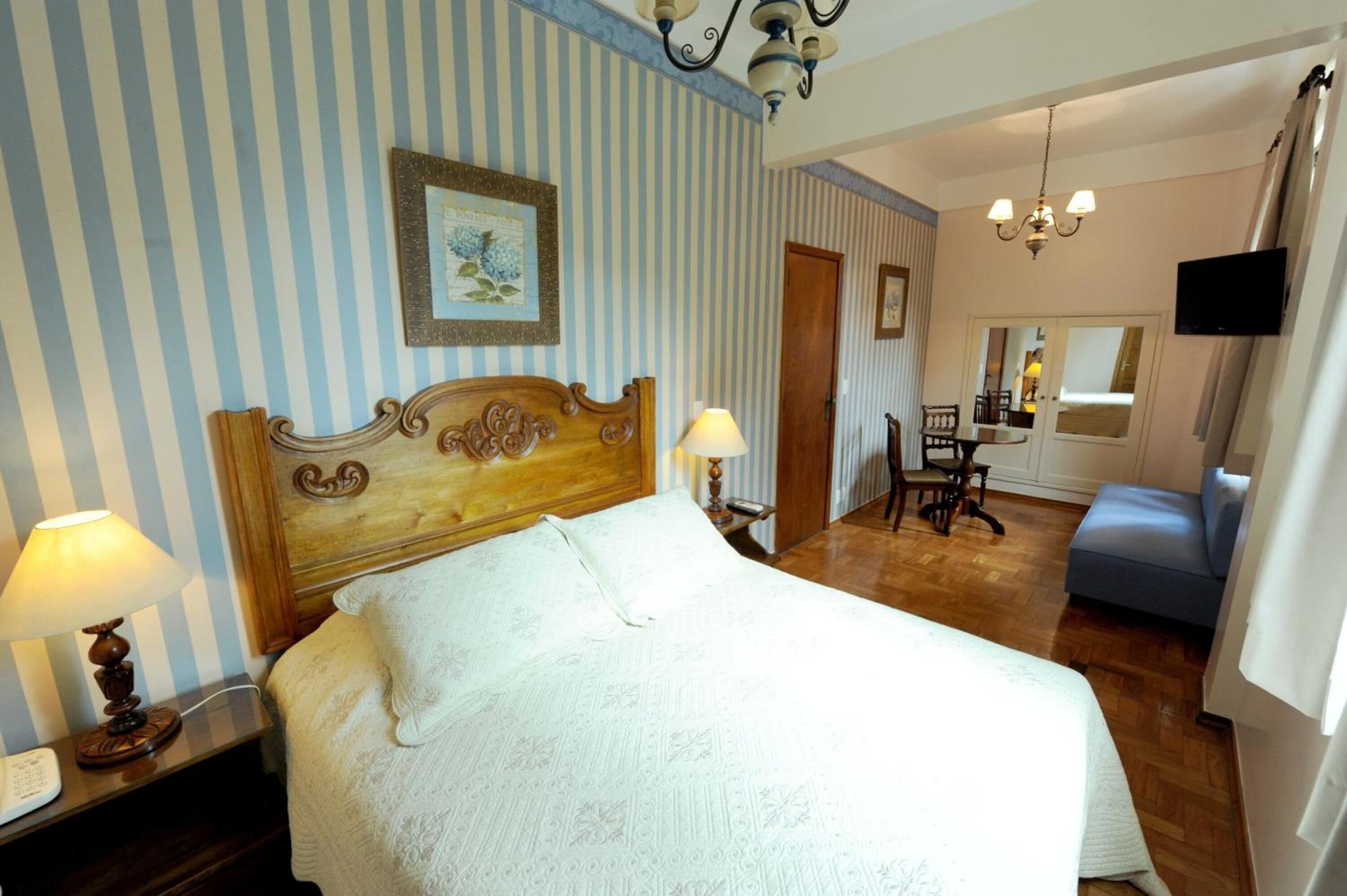 Hotelkamer met een groot bed, een houten hoofdbord, een bedlampje, een nachtkastje, een stoel, een televisie en een spiegel.