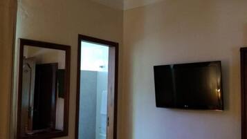 Ein Schlafzimmer mit Bett, Schreibtisch, Fernseher und einem durchgegangenen Tür erkennbaren Badezimmer.