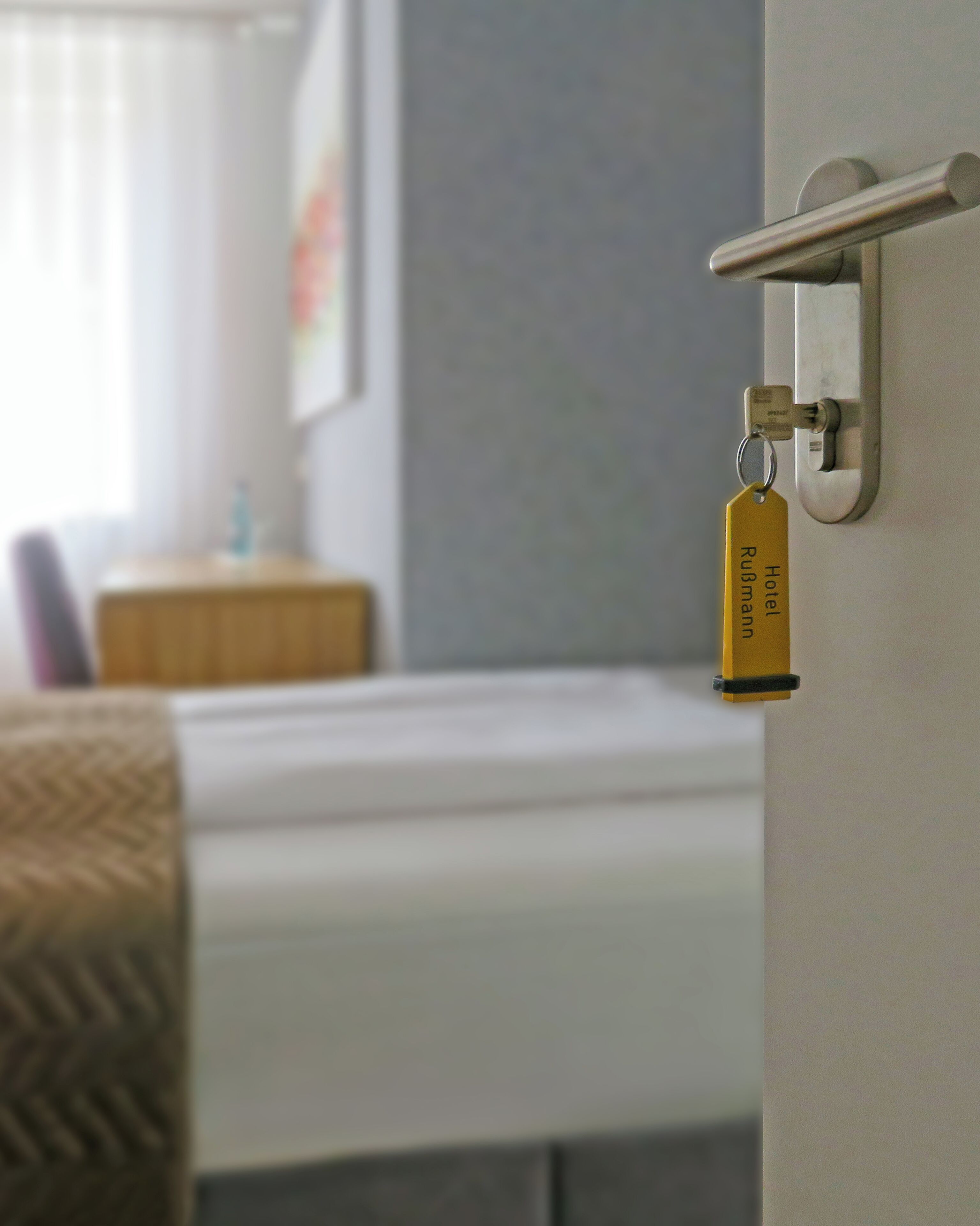 A hotel room with a bed, a bedside table, and a door with a keychain.