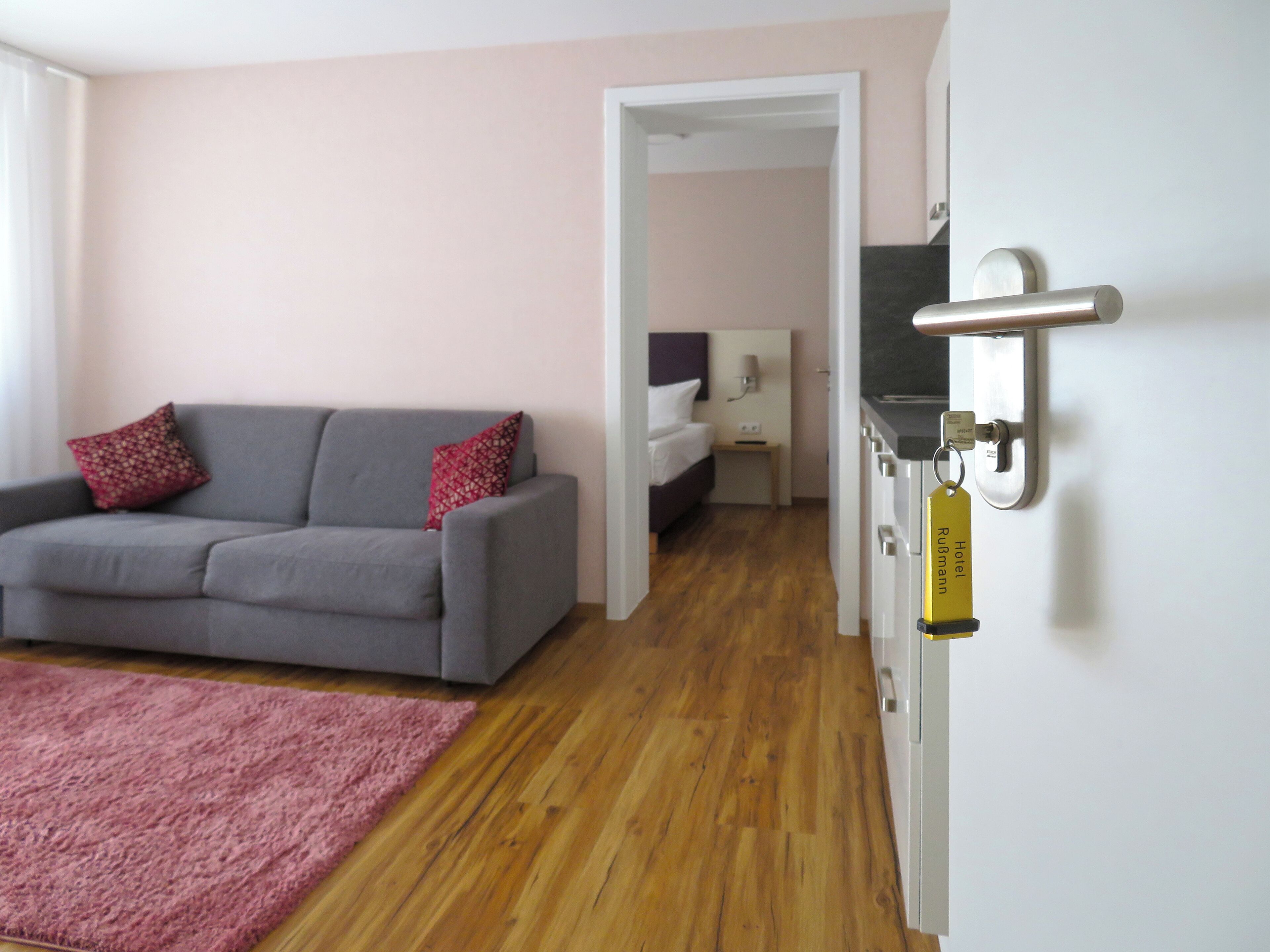 Una habitación de hotel moderna con un sofá gris, un tapete rosa y suelo de madera.