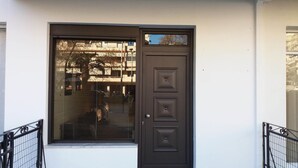 Una puerta marrón oscuro con un ventanal arriba, que refleja un edificio y árboles.