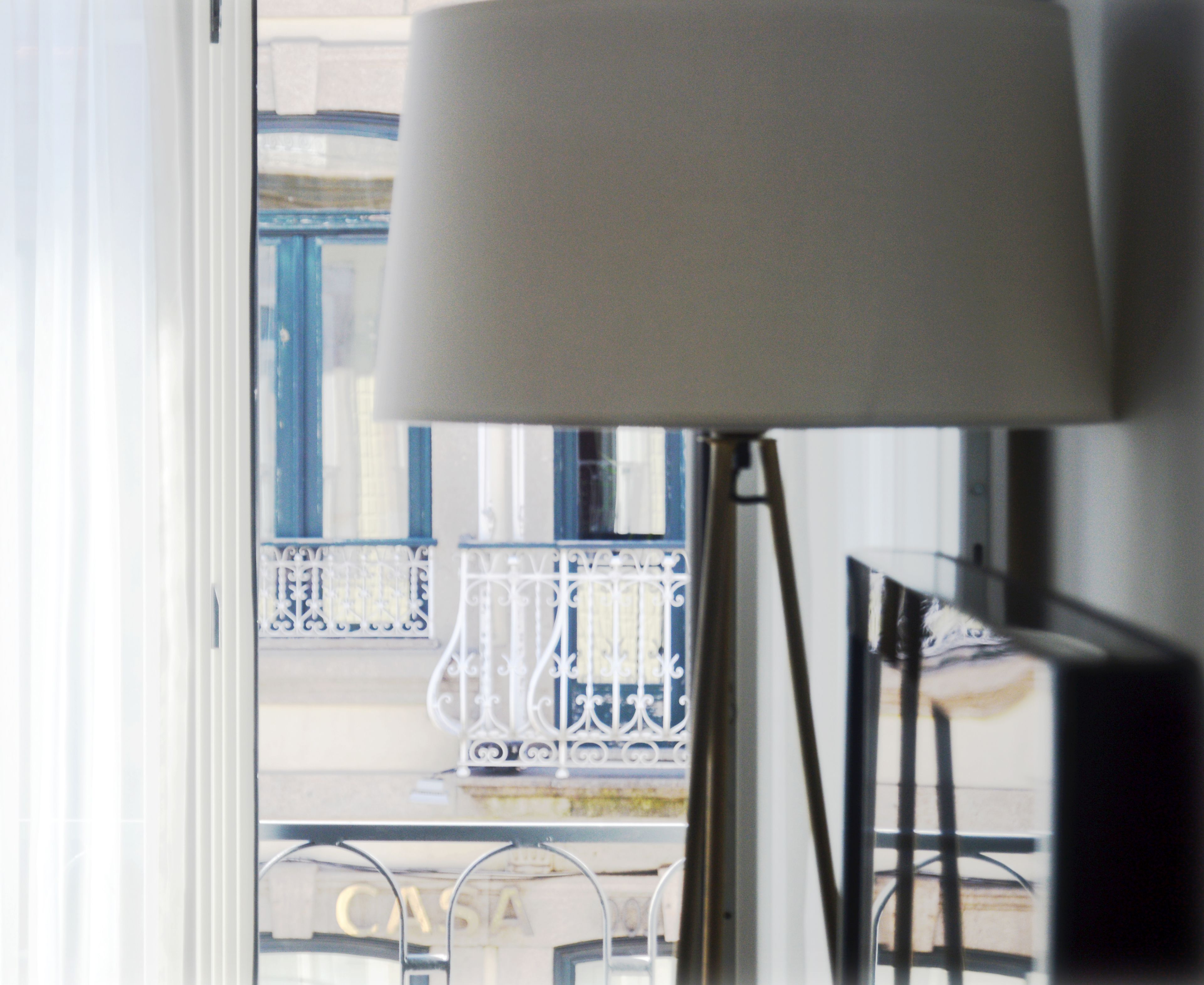 Eine Lampe mit weißem Lampenschirm, ein Balkon mit blauen Geländern und ein Gebäude mit der Aufschrift 'CASA'.